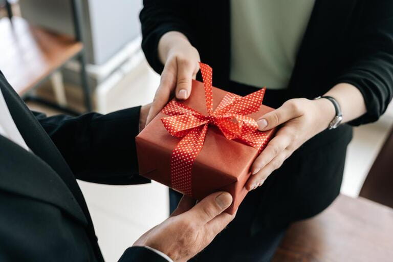 Close-up view of hands of unrecognizable woman giving red gift box tied to bow handed to man. Giving gifts during the Christmas, Happy New Year and Happy Birthday at office. Close-up view of hands of unrecognizable woman giving red gift box tied to bow handed to man. Giving gifts during the Christmas, Happy New Year and Happy Birthday at office.