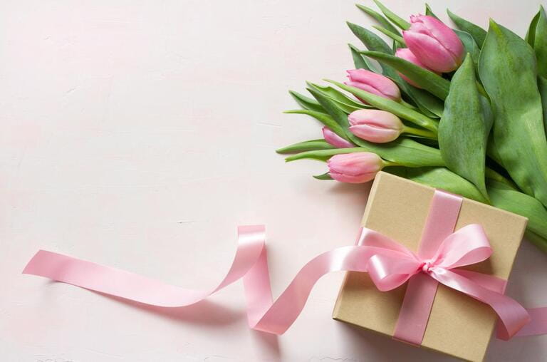 Gift box with long pink ribbon and tulips on light background Gift box with long pink ribbon and tulips on light background